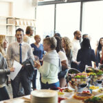 Ein Catering in Neubrandenburg bei einer Frimenfeier: Mitarbeiter stehen am Büffet und unterhalten sich bei gutem Essen.